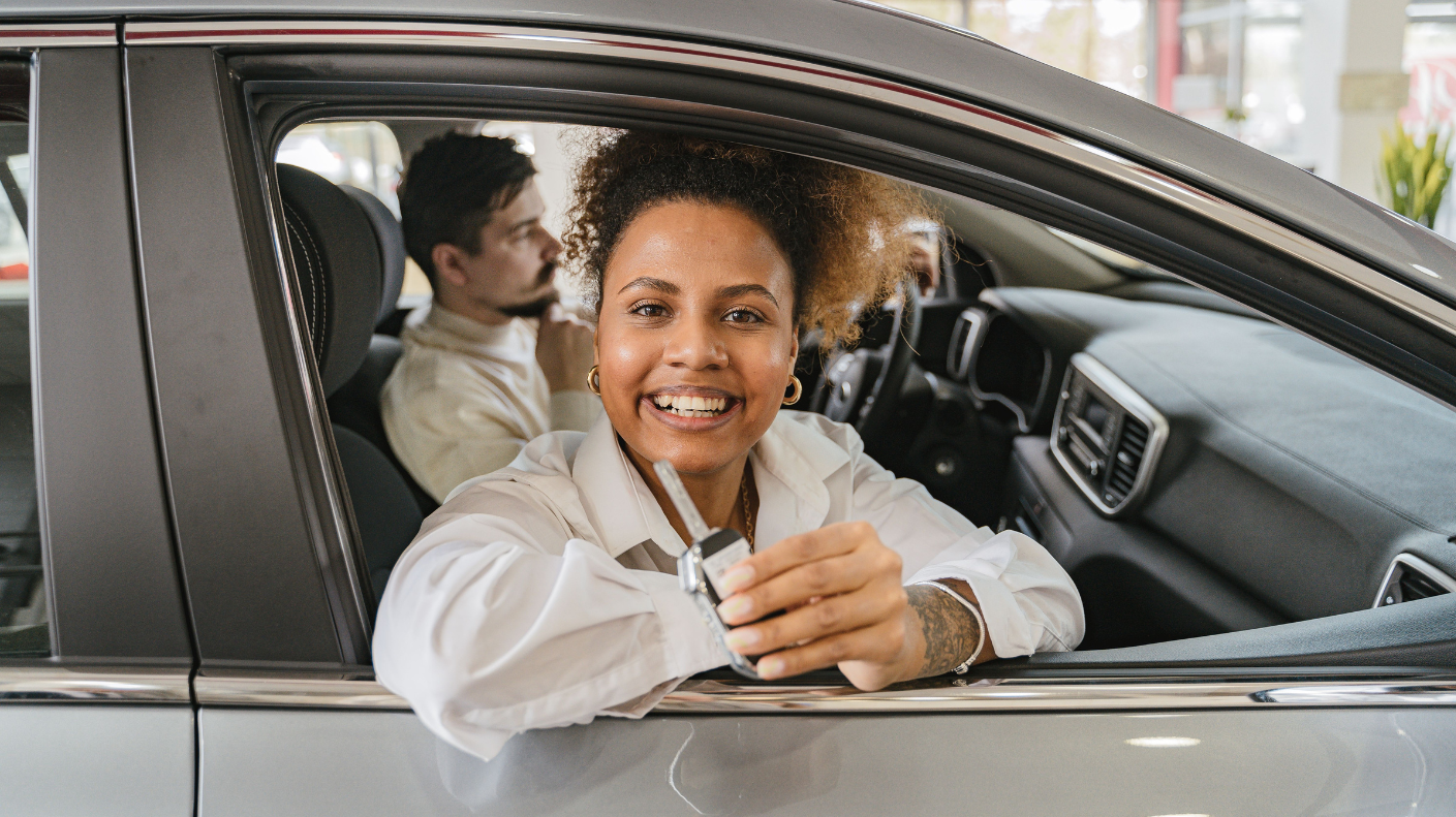 Happy woman smiling from the driver's seat of a new car at a dealership